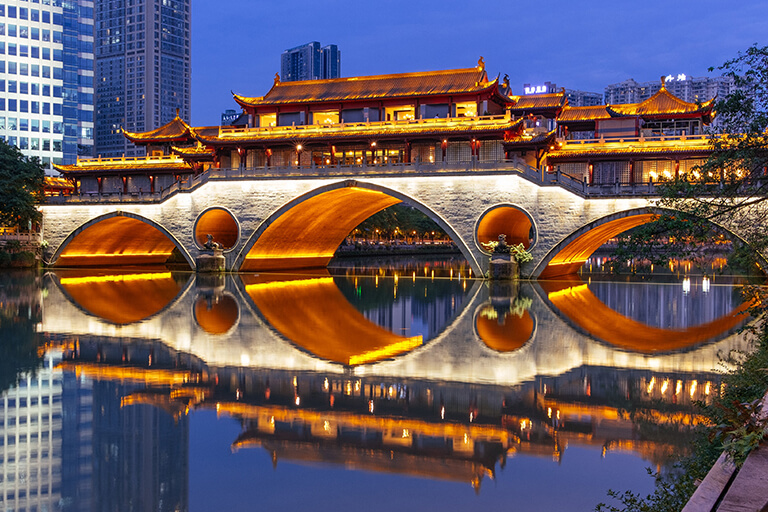 A bridge with a Chinese structure and buildings behind it.